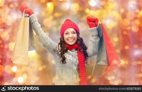 holidays, christmas, sale and people concept - happy smiling young asian woman in winter clothes with shopping bags over lights background