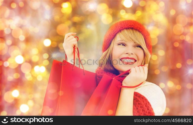 holidays, christmas, sale and people concept - happy smiling young woman in winter clothes with shopping bags over lights background