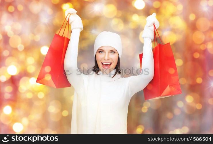 holidays, christmas, sale and people concept - happy smiling young woman in winter clothes with shopping bags over lights background