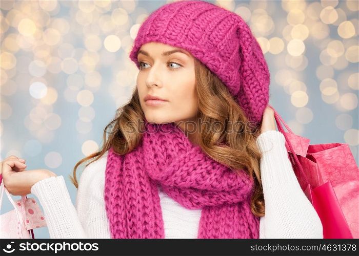 holidays, christmas, sale and people concept - happy young woman in winter clothes with shopping bags over lights background