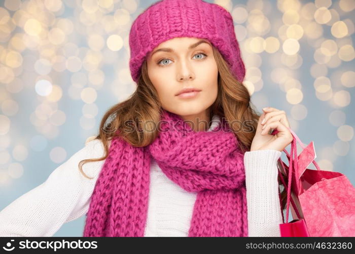 holidays, christmas, sale and people concept - happy young woman in winter clothes with shopping bags over lights background