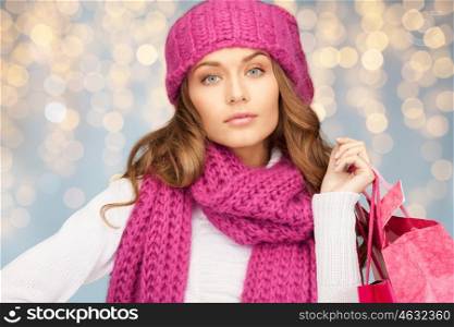 holidays, christmas, sale and people concept - happy young woman in winter clothes with shopping bags over lights background