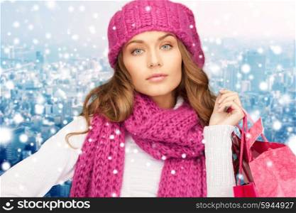 holidays, christmas, sale and people concept - young woman in winter clothes with shopping bags over snowy city background