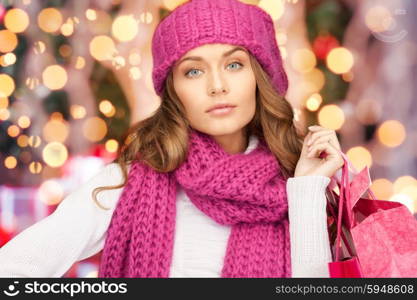 holidays, christmas, sale and people concept - young woman in winter clothes with shopping bags over lights background