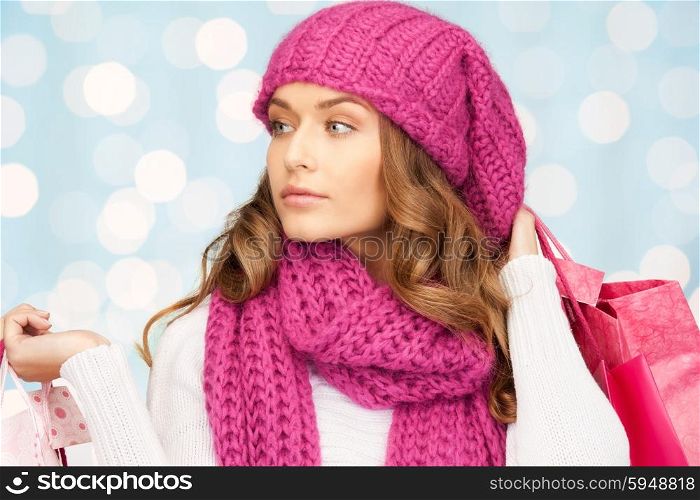 holidays, christmas, sale and people concept - young woman in winter clothes with shopping bags over lights background