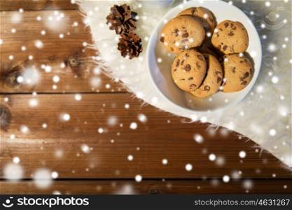 holidays, christmas, winter, advertisement and food concept - close up of cookies in bowl and cones on white fur rug on wooden board