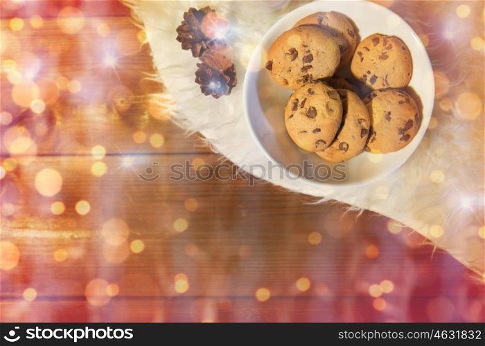 holidays, christmas, winter, advertisement and food concept - close up of cookies in bowl and cones on white fur rug over lights