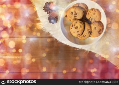 holidays, christmas, winter, advertisement and food concept - close up of cookies in bowl and cones on white fur rug over lights