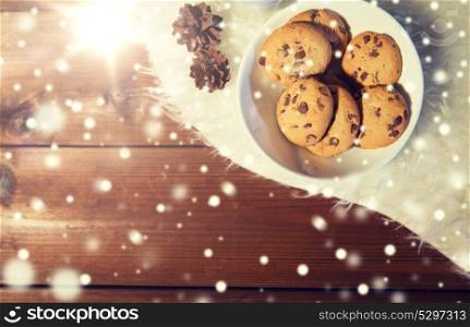 holidays, christmas, winter, advertisement and food concept - close up of cookies in bowl and cones on white fur rug on wooden board. close up of cookies in bowl and cones on fur rug