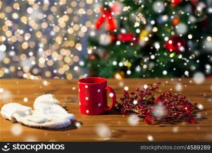 holidays, christmas, winter and drinks concept - close up of tea cup with mittens and christmas decoration on wooden table