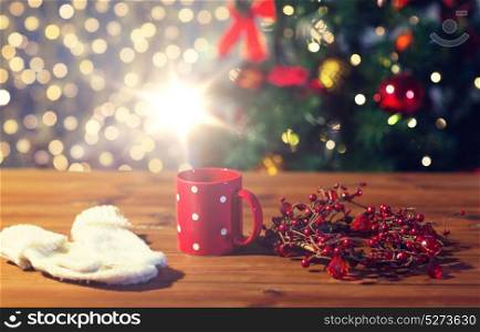 holidays, christmas, winter and drinks concept - close up of tea cup with mittens and christmas decoration on wooden table. tea cup with mittens and christmas decoration
