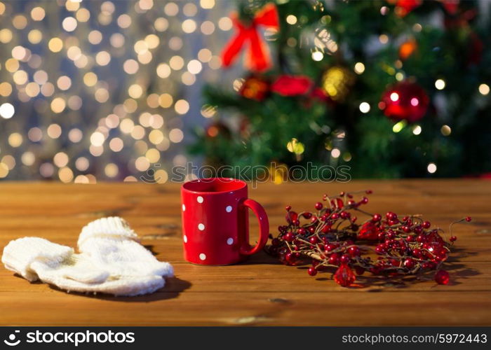 holidays, christmas, winter and drinks concept - close up of tea cup with mittens and christmas decoration on wooden table