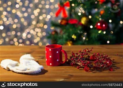 holidays, christmas, winter and drinks concept - close up of tea cup with mittens and christmas decoration on wooden table