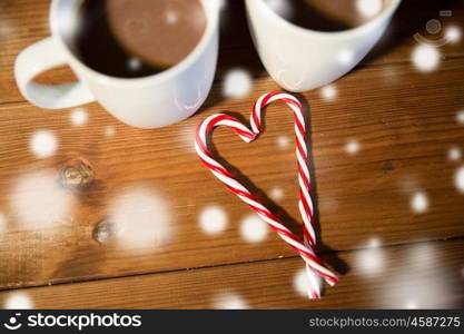 holidays, christmas, winter, food and drinks concept - close up of candy canes and cups with hot chocolate or cocoa drinks on wooden table