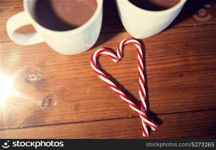 holidays, christmas, winter, food and drinks concept - close up of candy canes and cups with hot chocolate or cocoa drinks on wooden table. christmas candy canes and cups on wooden table