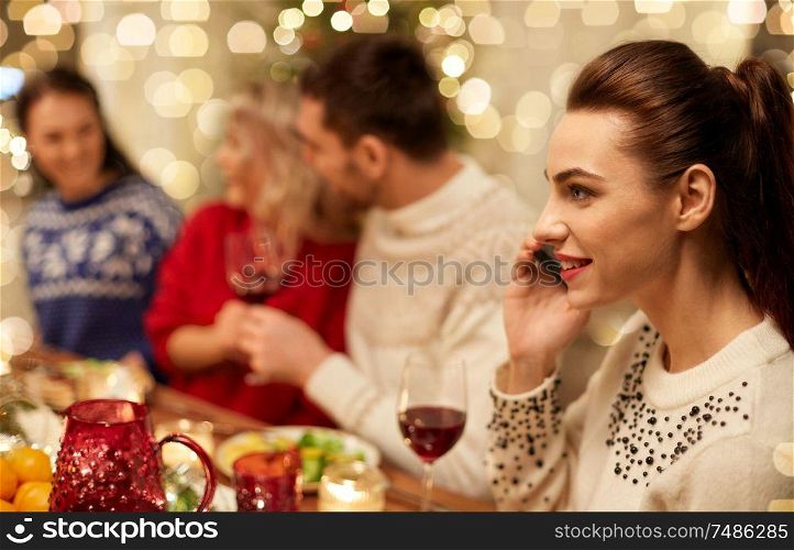 holidays, communication and celebration concept - close up of young woman calling on smartphone and having christmas dinner with friends at home. woman calling on smartphone at christmas dinner