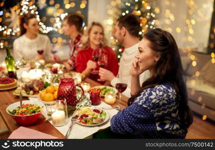 holidays, communication and celebration concept - happy young woman calling on smartphone and having christmas dinner with friends at home. woman calling on smartphone at christmas dinner