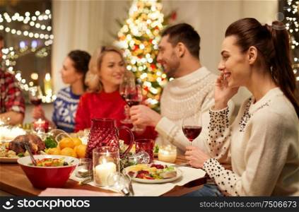 holidays, communication and celebration concept - happy young woman calling on smartphone and having christmas dinner with friends at home. happy friends having christmas dinner at home