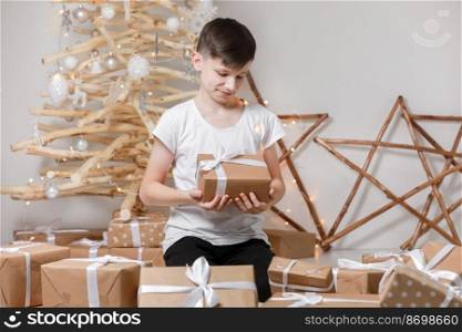 Holidays Concept. A smiling excited boy child by the wooden decoration Christmas tree, in his hands he holds a big gift box. new Year’s Eve and Christmas, waiting for a miracle.. Holidays Concept. A smiling excited boy child by the wooden decoration Christmas tree, in his hands he holds a big gift box. new Year’s Eve and Christmas, waiting for a miracle