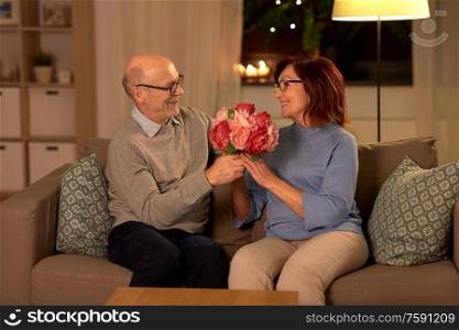 holidays, couple and people concept - happy senior man giving with bunch of flowers to smiling woman at home. happy senior couple with bunch of flowers at home