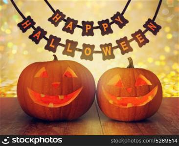 holidays, decoration and celebration concept - jack-o-lantern or pumpkins and happy halloween festive garland or banner over lights background. carved pumpkins and happy halloween garland