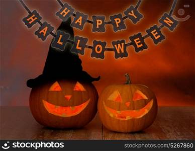 holidays, decoration and celebration concept - jack-o-lanterns or pumpkins in witch hat and happy halloween festive garland or banner over dark background. carved pumpkins and happy halloween garland