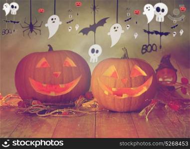 holidays, decoration and celebration concept - jack-o-lanterns or pumpkins in witch hat and halloween festive garland over gray background. carved pumpkins in witch hat and halloween garland