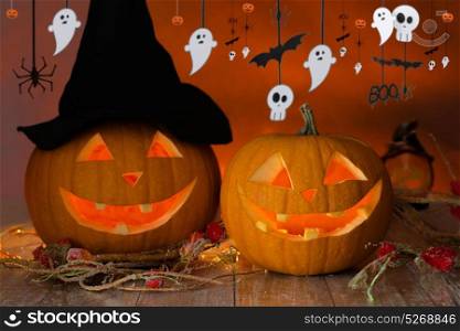 holidays, decoration and celebration concept - jack-o-lanterns or pumpkins in witch hat and halloween festive garland over dark background. carved pumpkins in witch hat and halloween garland