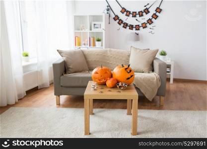 holidays, decoration and party concept - home room with jack-o-lantern or carved pumpkin, halloween decorations and treats on wooden table. jack-o-lantern and halloween decorations at home