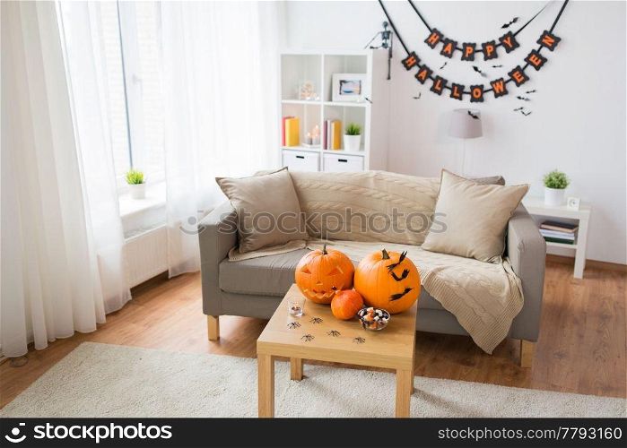 holidays, decoration and party concept - home room with jack-o-lantern or carved pumpkin, halloween decorations and treats on wooden table. jack-o-lantern and halloween decorations at home