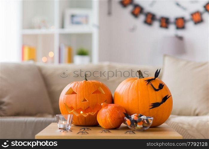 holidays, decoration and party concept - jack-o-lantern or carved pumpkin with halloween decorations and treats on wooden table at home room. jack-o-lantern and halloween decorations at home