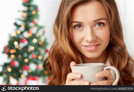 holidays, drink, winter and people concept - close up of happy young woman with cup of coffee or tea over christmas tree lights background. close up of woman with tea cup over christmas tree