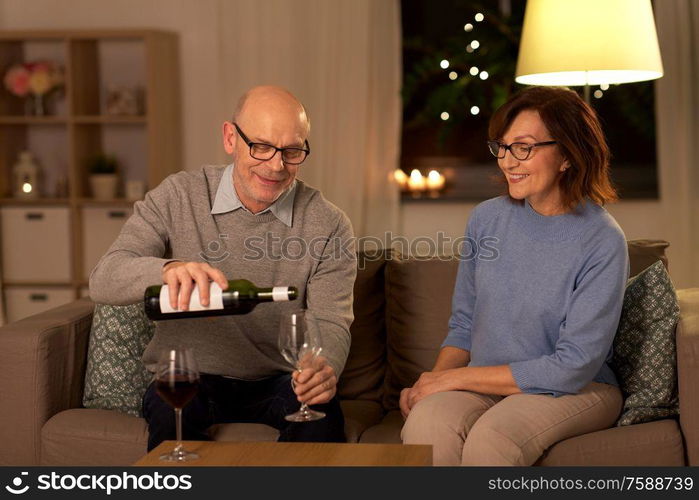 holidays, drinks and people concept - happy smiling senior couple drinking red wine at home in evening. happy senior couple drinking red wine at home