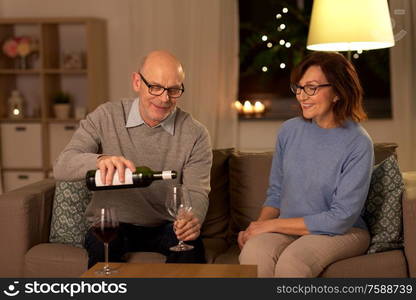 holidays, drinks and people concept - happy smiling senior couple drinking red wine at home in evening. happy senior couple drinking red wine at home