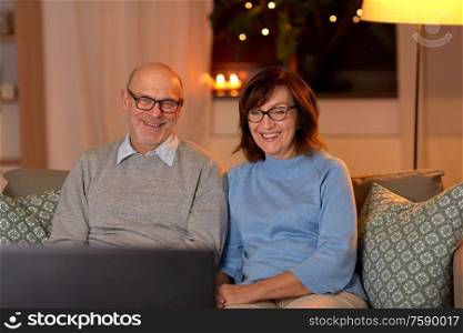 holidays, drinks and people concept - happy smiling senior couple watching tv at home in evening. happy senior couple watching tv at home