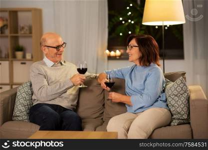 holidays, drinks and people concept - happy smiling senior couple with glasses of red wine at home in evening. happy senior couple with glasses of red wine