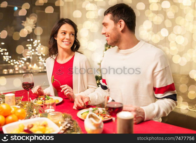 holidays, eating and celebration concept - happy couple having christmas dinner at home. happy couple eating at christmas dinner