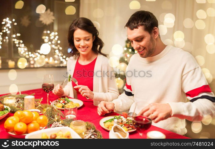 holidays, eating and celebration concept - happy couple having christmas dinner at home. happy couple eating at christmas dinner