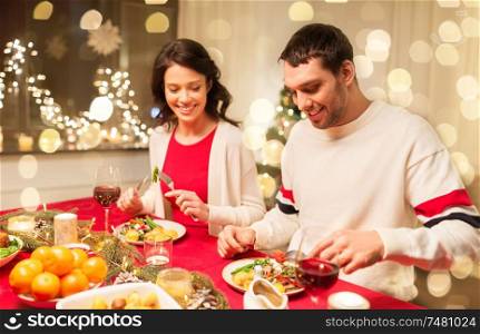 holidays, eating and celebration concept - happy couple having christmas dinner at home. happy couple eating at christmas dinner
