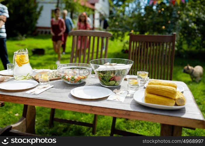 holidays, eating, mealtime and food concept - people coming to served table with dinner at summer garden party. people coming to table with food at summer garden