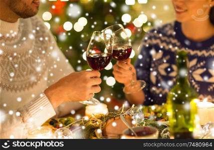 holidays, family and celebration concept - close up of happy couple having christmas dinner, drinking red wine and clinking glasses over snow. happy couple drinking red wine at christmas dinner