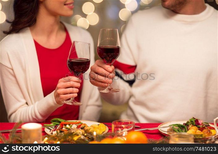 holidays, family and celebration concept - close up of happy couple having christmas dinner at home and drinking red wine. close up of couple drinking red wine on christmas
