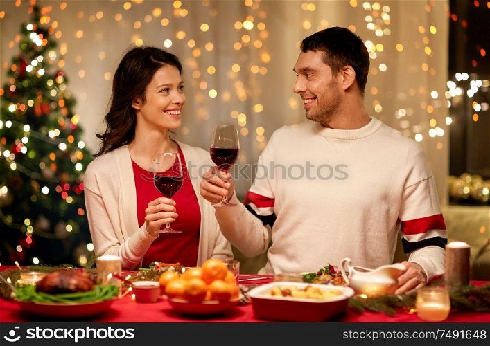 holidays, family and celebration concept - happy couple having christmas dinner at home and drinking red wine. happy couple drinking red wine at christmas dinner