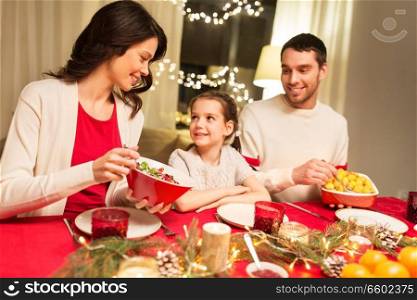 holidays, family and celebration concept - happy mother, father and little daughter having christmas dinner at home. happy family having christmas dinner at home