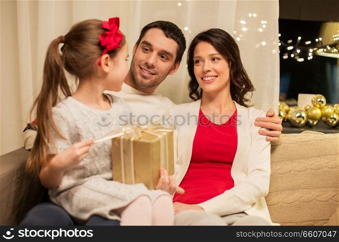 holidays, family and celebration concept - happy mother, father and little daughter with christmas present at home. happy family with christmas present at home
