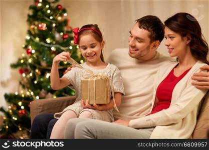 holidays, family and celebration concept - happy mother, father and little daughter opening christmas present at home. happy family with christmas present at home