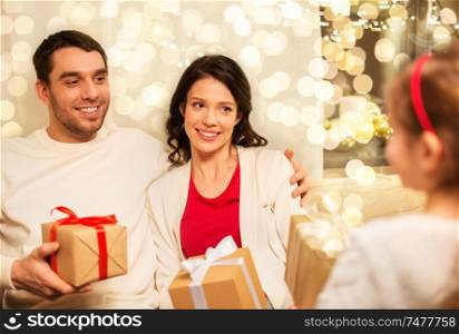 holidays, family and celebration concept - happy mother, father and little daughter giving christmas presents at home. happy family giving christmas presents at home