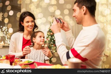holidays, family and celebration concept - happy mother, father and little daughter having christmas dinner and taking picture by smartphone at home. happy family taking picture at christmas dinner