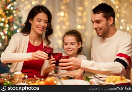 holidays, family and celebration concept - happy mother, father and little daughter with drinks toasting at home christmas dinner. happy family having christmas dinner at home