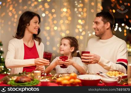 holidays, family and celebration concept - happy mother, father and little daughter with drinks toasting at home christmas dinner. happy family having christmas dinner at home